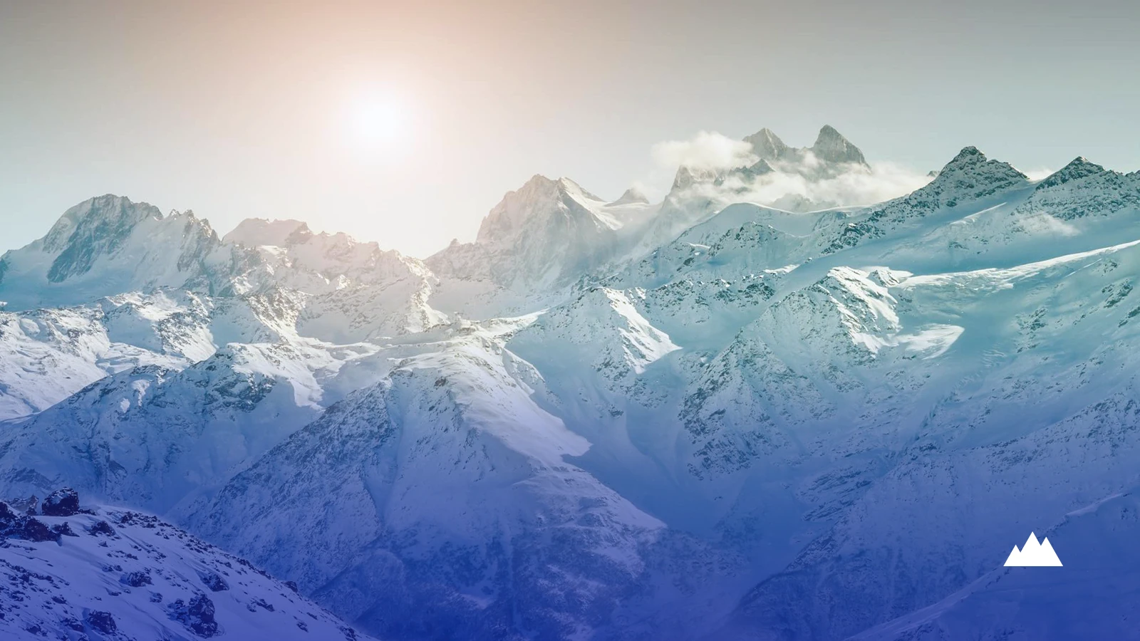 A high snow-covered mountain range under low sun, with cloud gathering along the ridgeline